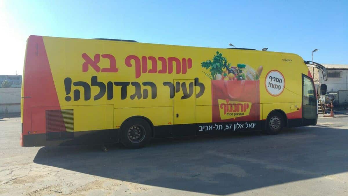 שילוט אוטובוסים לרשת יוחננוף – עיטוף אוטובוס מלא בצבע צהוב בולט עם הכיתוב "יוחננוף בא לעיר הגדולה" וצילום סל קניות עמוס בתוצרת טרייה.